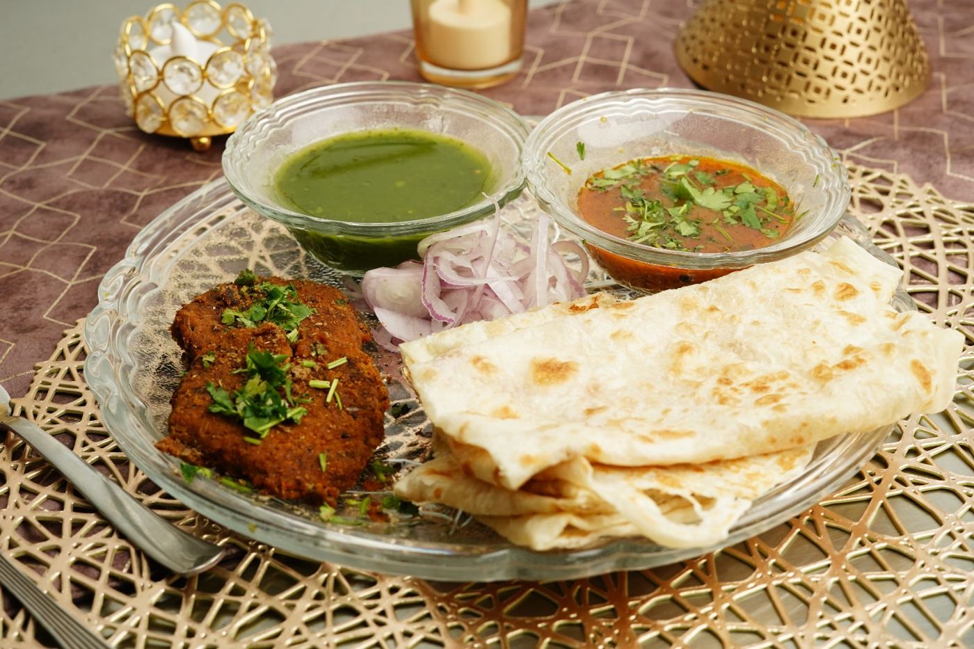 Veg kabab paratha with green chutney, gravy and onions on a glass plate