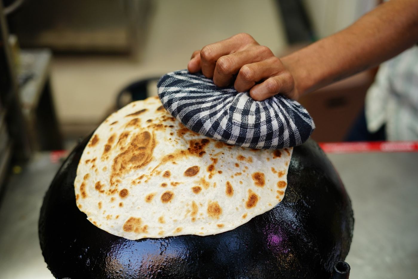 Roomali paratha on the upturned tawa, pressed with a checked cloth